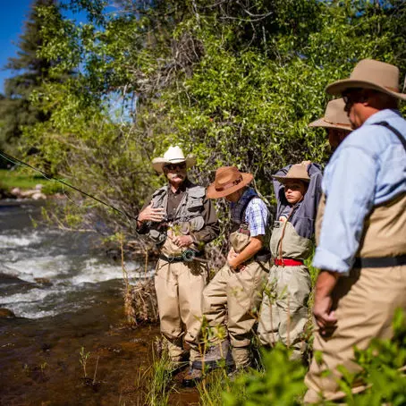 Several people in hats and waders stand by a river.