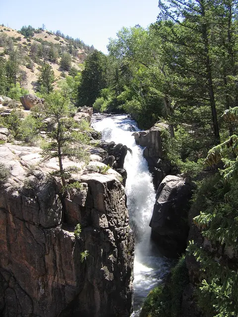 A waterfall flows through a rocky gorge surrounded by trees and mountains.