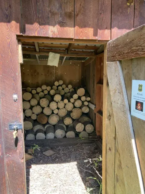 A wooden shed is filled with stacked logs for firewood.