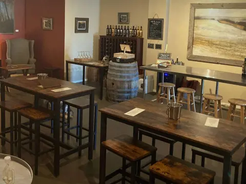 An interior view of a tasting room with wooden tables, stools, and wine displays.