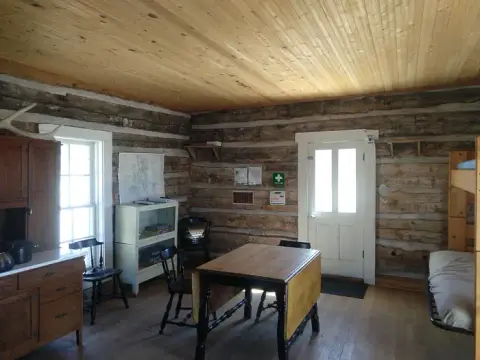 An interior view of a rustic log cabin with a table, chairs, bunk beds, and wooden walls.