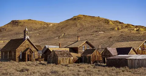 A collection of historic wooden buildings in a desert landscape with hills in the background.