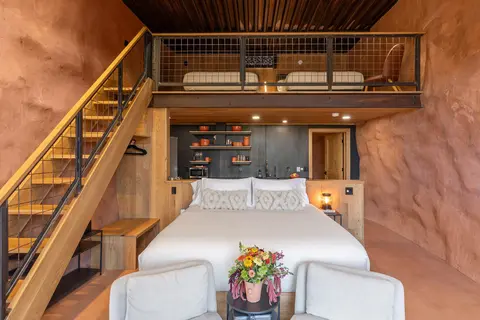 A modern interior hotel room with a loft bed and rock wall.