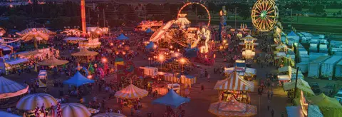 An aerial night view of a brightly lit carnival with rides and crowds.
