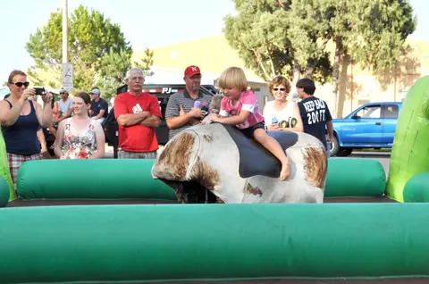 A child rides a mechanical bull surrounded by onlookers.