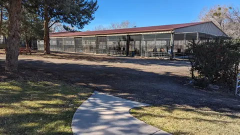 Exterior view of a long, open-air livestock barn with chain-link fencing and a red roof.