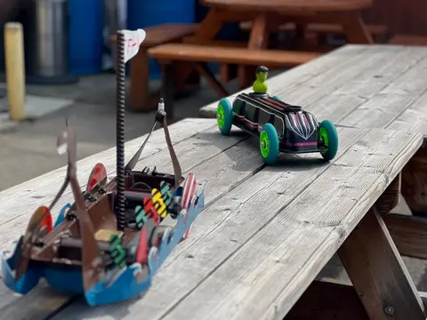 Two toy vehicles sit on a wooden picnic table outdoors.