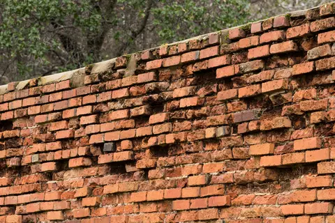 A weathered brick wall with missing mortar and damaged bricks.