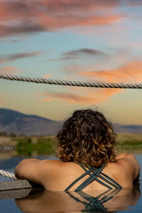 A woman looks out over a landscape at sunset from a pool.