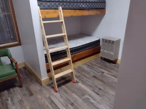A photograph shows the interior of a room with bunk beds, a wooden ladder, a chair, and a small AC unit.