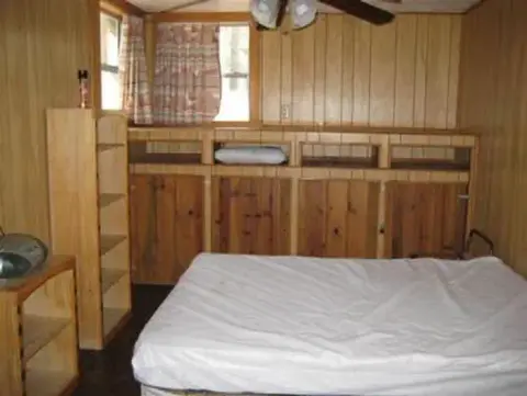 A photo showing the interior of a room with wood paneling and a bed.