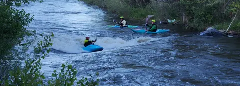 Three people kayaking through river rapids.