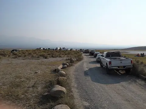 A line of parked vehicles and tents along a dirt road in a desert landscape.