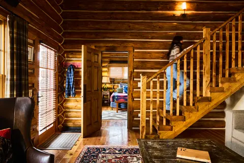 A person walks up the wooden stairs in a rustic log cabin interior.