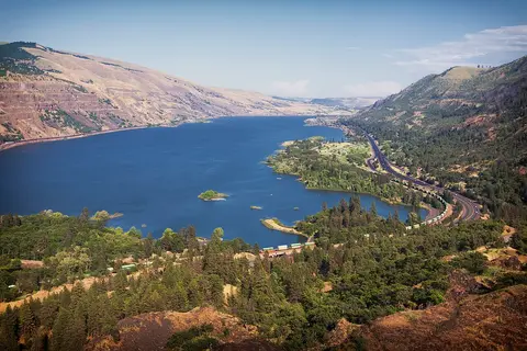 An elevated scenic view of a wide river flanked by mountains and forests.