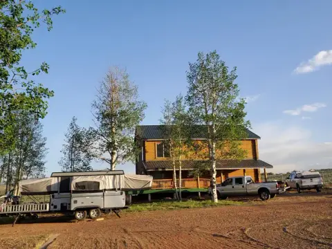 A two-story log cabin with a pop-up camper and pickup trucks parked outside.