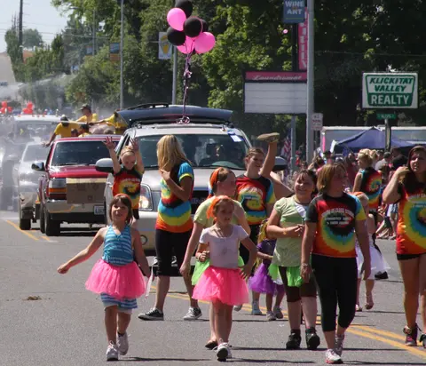 A group of children in matching outfits walking in a street parade.
