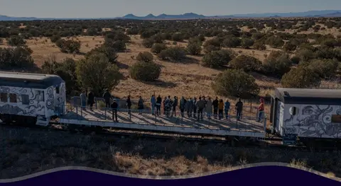 People stand on a flatbed train car viewing a desert landscape.