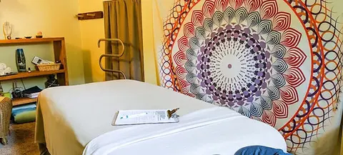 An interior shot of a massage table with a large colorful tapestry on the wall.