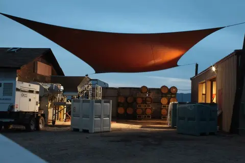 An exterior view of a facility with stacked barrels beneath a large sun shade.