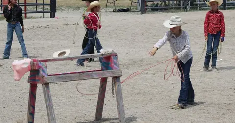 Children practice roping skills in an outdoor arena using a wooden dummy calf.