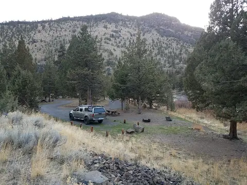 A truck parked at a campsite near trees and hills.