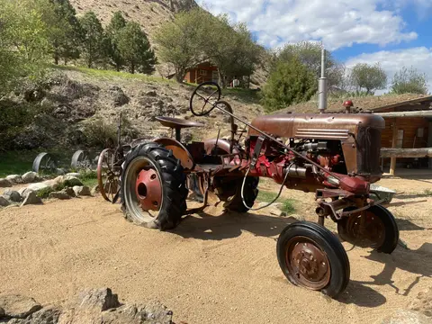 An old rusty tractor sits parked on a dirt ground outdoors.