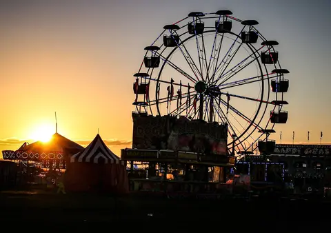 A carnival with a Ferris wheel and tents at sunset.