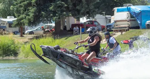 People riding snowmobiles on water near a campground.