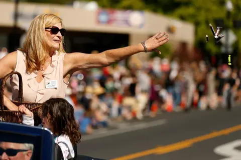 A woman throws candy to the crowd from a moving vehicle.