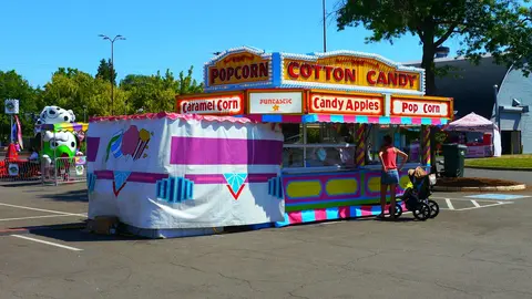 A colorful food stand at an outdoor event sells popcorn and cotton candy.