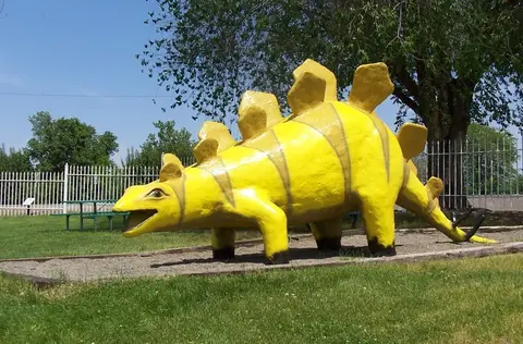 A yellow and brown dinosaur statue stands in a grassy park.