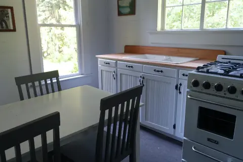 A bright interior view of a rustic kitchen with white cabinets and a dining table.