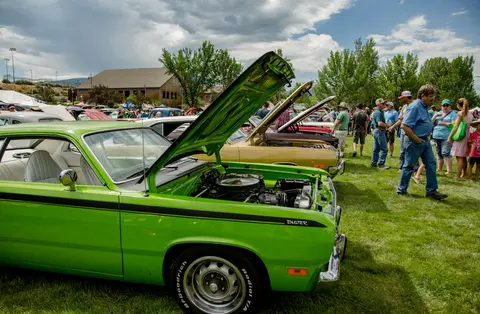A bright green classic car with its hood open is displayed at an outdoor car show.