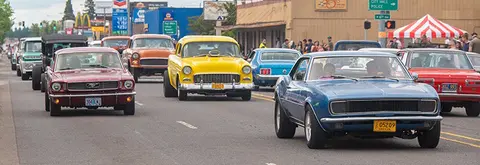A parade of classic cars drives down a town street.