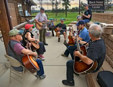 A group of people play acoustic guitars and a fiddle outside a community center.