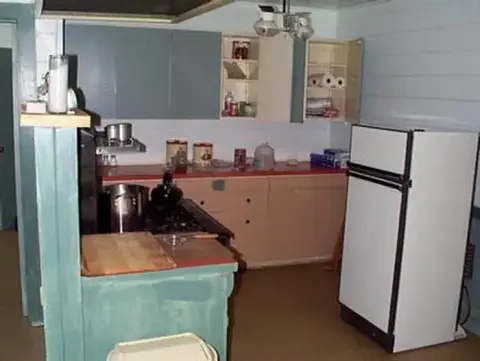 A photo of an interior kitchen showing cabinets, countertops, and a refrigerator.