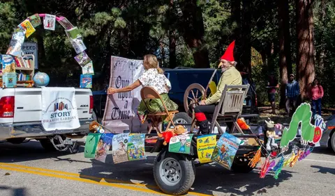 People ride on a book-themed parade float attached to a pickup truck.