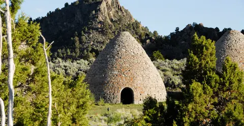 A stone beehive oven stands outdoors against a mountain backdrop.