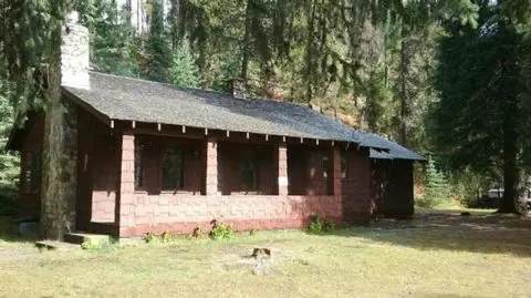 A rustic wooden cabin with a stone chimney sits among trees.