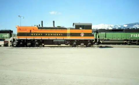 A train locomotive is parked on the tracks with mountains in the background.
