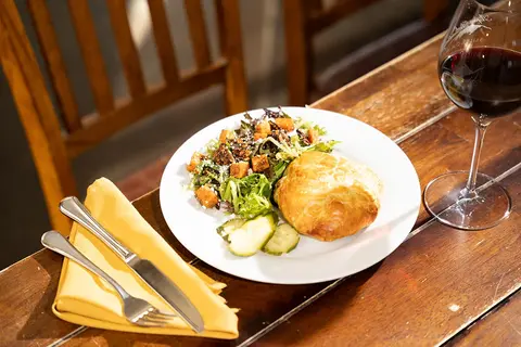 A plate of food with salad, a pastry, and a glass of red wine on a wooden table.