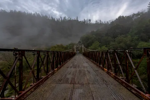 A bridge spans across a landscape with foggy trees and an overcast sky.