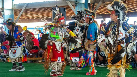 People perform in traditional regalia under an outdoor shelter.