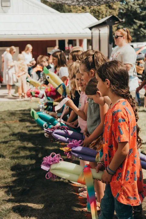 A line of children holding pool noodle craft creations outside a building.