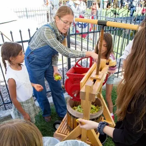 A woman demonstrates a cider press for children.