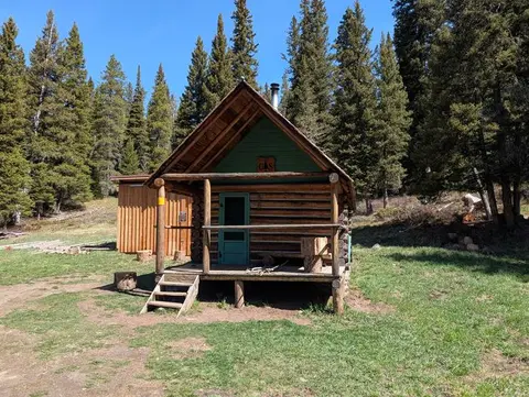 A log cabin stands in a clearing surrounded by tall pine trees.