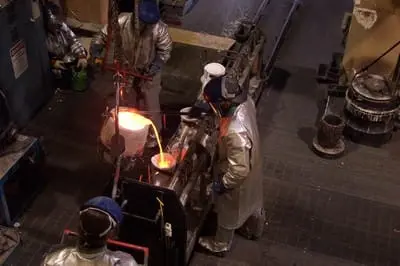Workers in protective gear pour molten metal in an industrial setting.