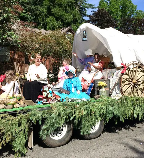 People ride on a parade float decorated to look like a covered wagon.