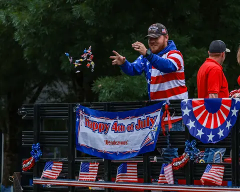 A man throws candy from a festive parade float decorated with American flags.